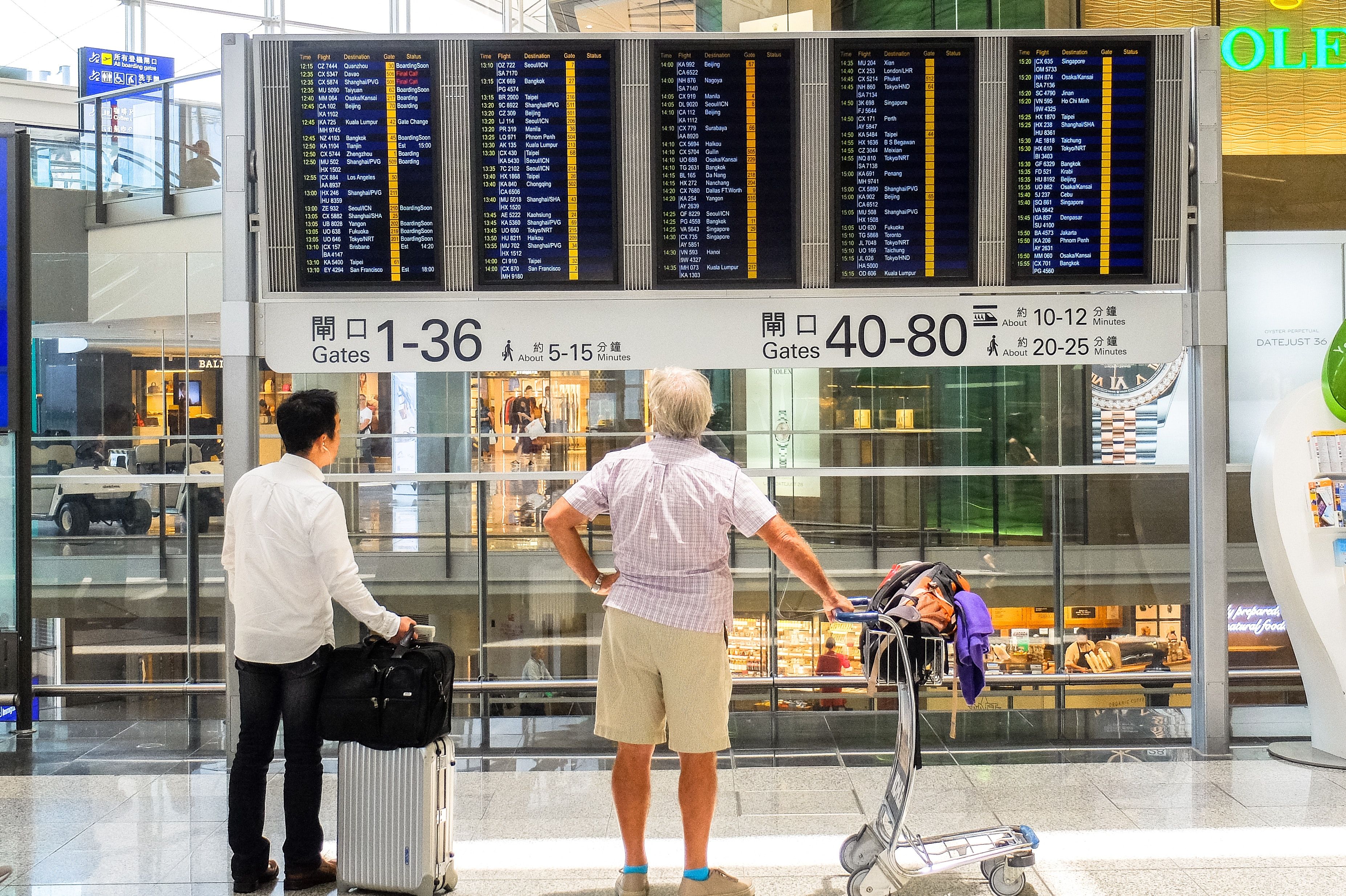 Zwei Männer mit Gepäck stehen vor einer Flugtafel in einem Flughafen